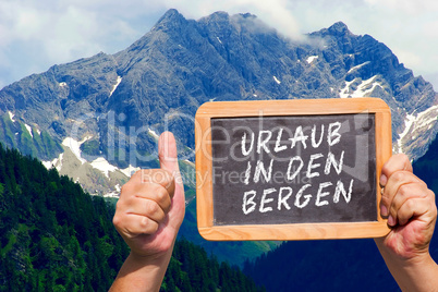 Hände halten Tafel mit Text: Urlaub in den Bergen