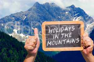 Hände halten Tafel mit Text: Holidays in the Mountains