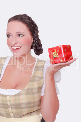 Junge Frau im Dirndl und geflochtenen Haaren hat ein Geschenk auf der flachen Hand