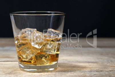 Whisky im Glas mit Eiswürfeln auf Holzbrett