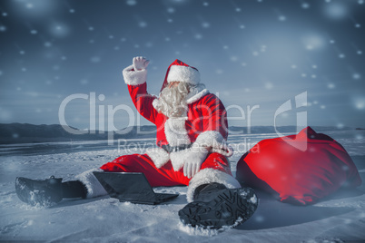 Santa Claus sitting in the snow with a laptop and looking away f