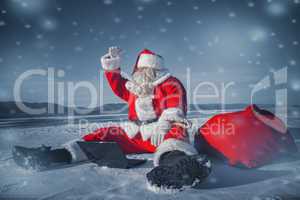 Santa Claus sitting in the snow with a laptop and looking away f
