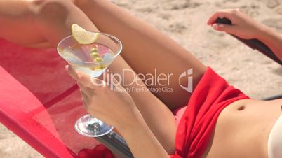 Young woman holding martini cocktail with olives on summer beach