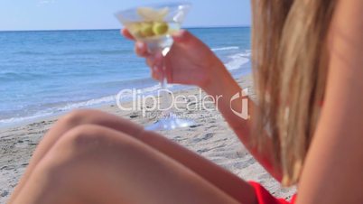 Young woman drinking martini cocktail on the summer sandy beach