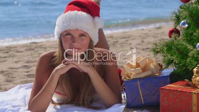Smiling pretty woman with gifts under decorated Christmas tree on tropical beach