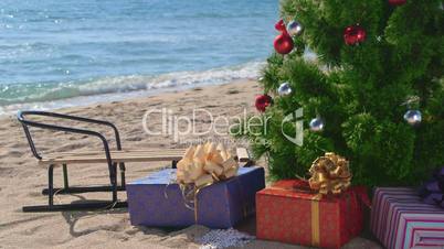 Christmas beach holidays - decorated tree with gift boxes and sledge
