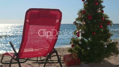 Lounge chair and Christmas tree with gift boxes on sandy beach