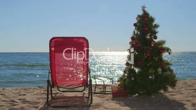 Lounge chair and Christmas tree with gift boxes on sandy beach