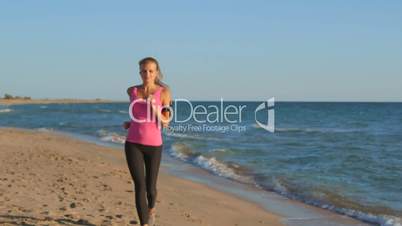 Fitness girl jogging on beach listening music during workout