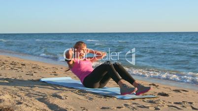 Fitness routine for women - athletic girl doing abdominal crunch on the beach