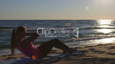 Fitness routine for women - athletic girl doing abdominal crunch on the beach