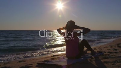 Fitness athletic woman doing abdominal crunch during workout on the beach at sunset