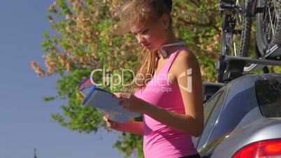 Young fit woman driver stand near car and look on map for directions