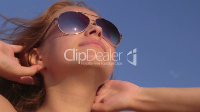 Face of young girl in sunglasses sunbathing on the beach