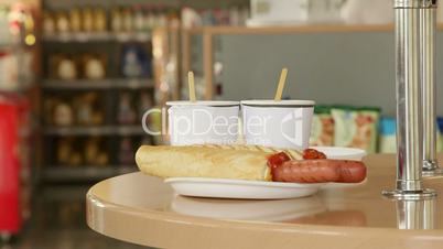 Hot dogs and cups of coffee on the table in convenience store
