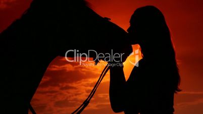 Young woman rider kissing her horse at sunset