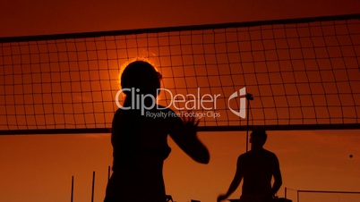 People enjoy playing volleyball on beach at sunset