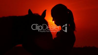 Silhouette of young girl rider with horse against sun and dramatic sky