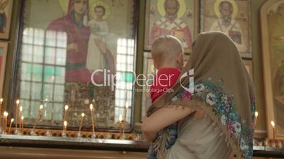 Mother with child lighting prayer candle in Christian Orthodox Church