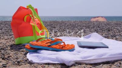 Beach bag flip flops towel and tablet computer at summer shore