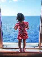 Baby looking to the sea from a big ship window