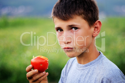 Young boy eating fresh tomato