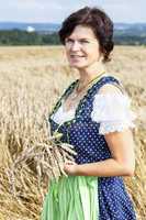 Bavarian woman in dirndl holds heads of grain in wheat field