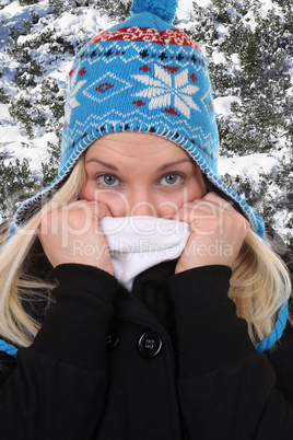 Junge Frau im Winter beim Frieren mit Mütze im Wald