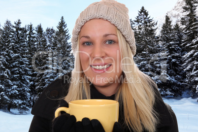 Junge blonde Frau draußen beim Trinken einer Tasse Tee im Winte