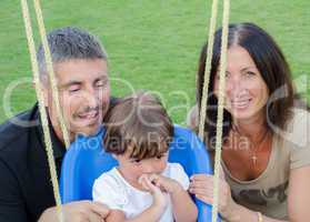 Baby girl on the swing with her parents smiling