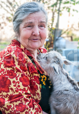 Senior woman holding a goatling on a background of his home