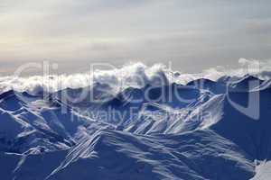 Evening snowy mountains in mist and sunlight clouds