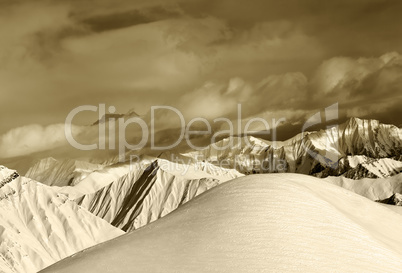 Sepia off-piste snowy slope and cloudy mountains