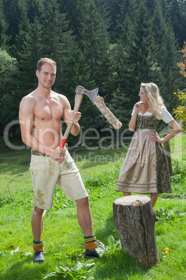 Szene eines bayerischen Pärchen in Trachtenbekleidung beim Holzhacken
