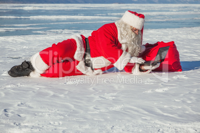 Santa Claus lying on the snow, looking at laptop news