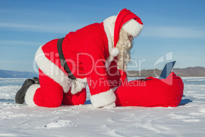 Santa Claus lying on the snow, looking at laptop news