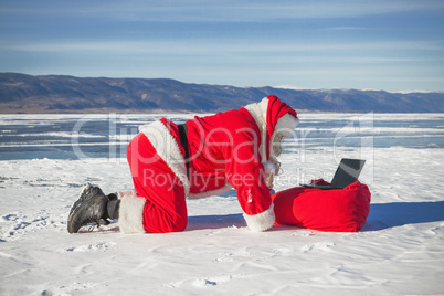 Santa Claus lying on the snow, looking at laptop news