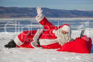 Santa Claus lying on the snow, looking at laptop news