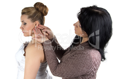 Bridesmade helping bride to wear earrings
