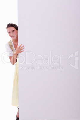 Junge Frau im Dirndl versteckt sich hinter einer Wand