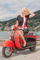 Blondes Model in einem Sommerkleid auf einem Motorroller