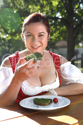 Woman in typical Bavarian costume eats bread with chives in a Ba