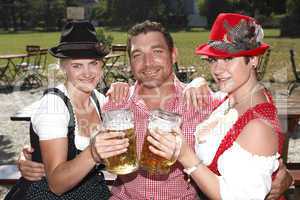 Three Bavarians in traditional costumes sitting in a beer garden