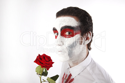 Man with white mascara and bloody shirt holds red rose