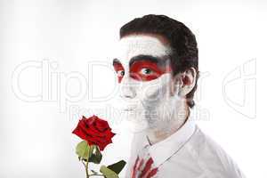 Man with white mascara and bloody shirt holds red rose