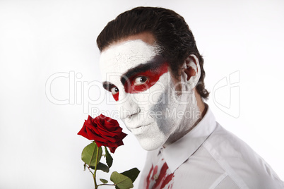 Man with white mascara and bloody shirt holds red rose