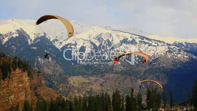 Locked-on shot of paragliders over mountain range