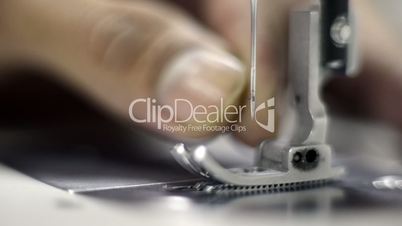 Locked-on shot of tailor inserting thread into a needle on sewing machine