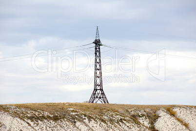 High voltage line and electricity pylon on coastline of river.