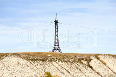 High voltage line and electricity pylon on coastline of river.